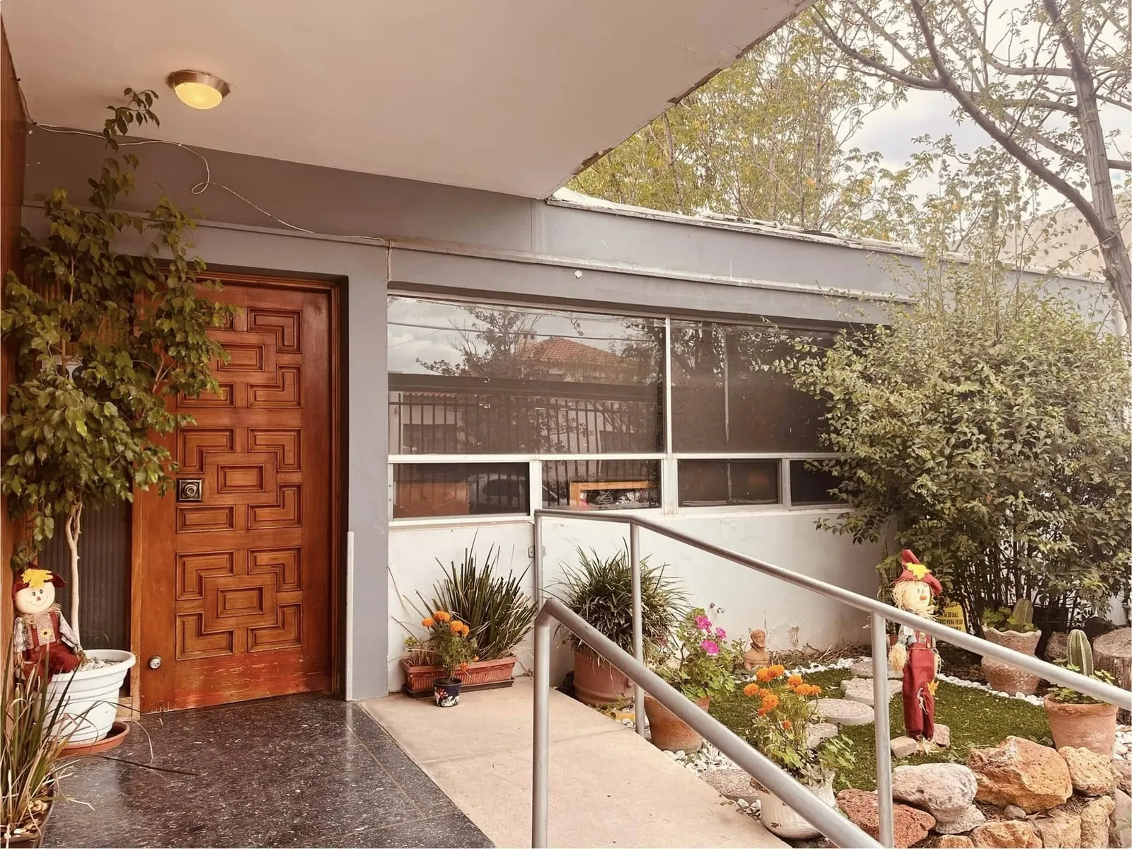 Fachada y entrada principal de Asilo Los Geranios con puerta de madera, rampa y jardín en Chihuahua